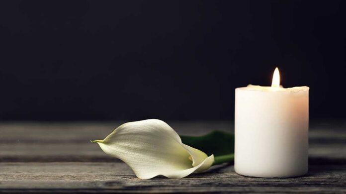 1658063071 featured image White candle and lily on a wooden surface.