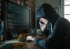 Hacker in hood using computer and phone analyzing cod