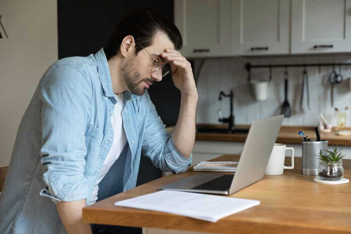 1783837082 Man stressing over work on laptop at kitchen table
