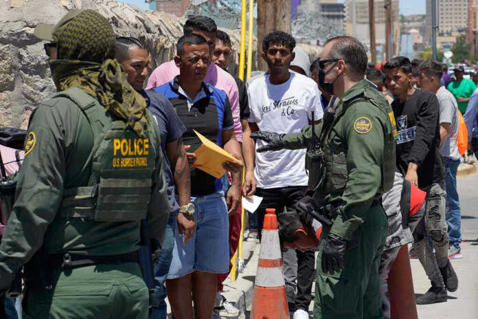 2300859029 Border patrol agents inspecting group of individuals in line
