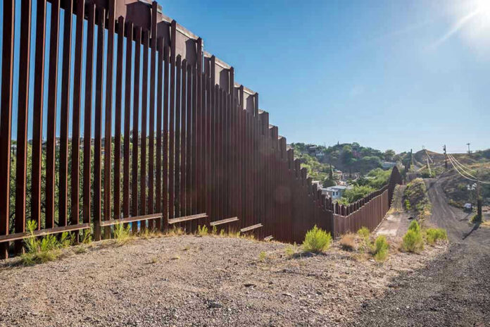 657897121 Tall metal border wall with rural landscape