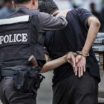 Police officer arrests handcuffed person.