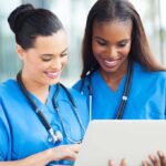 Red States Defy Norms in Health Revolution Two nurses in blue scrubs smiling while looking at a tablet