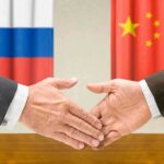 Two hands shaking in front of Russian and Chinese flags