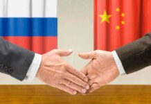 Two hands shaking in front of Russian and Chinese flags