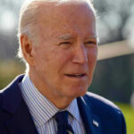 Elderly man in suit outside in daylight.