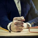 A man's clenched fist resting on a desk with office supplies nearby