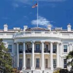 Permanent Layoffs ROCK Federal Workforce-Trump GIVES GO-AHEAD! The White House with the American flag flying against a blue sky