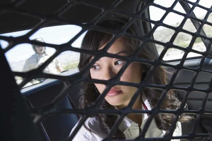 A woman sitting in the back of a police car, looking through a protective mesh barrier