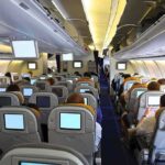 Interior view of an airplane with passengers seated and using in-flight entertainment screens