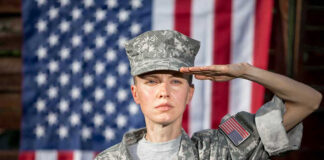 Soldier saluting in front of American flag backdrop.