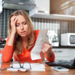 $1 Answer Turns Into Costly Nightmare Woman looking stressed holding bills in kitchen
