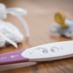 White House Baby Bombshell—Modern History Made A pregnancy test next to a pacifier and a knitted baby hat on a wooden surface
