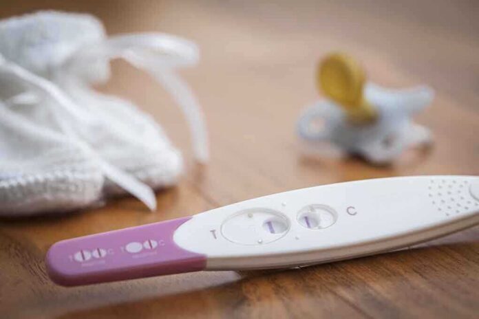 A pregnancy test next to a pacifier and a knitted baby hat on a wooden surface