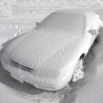 A car completely covered in snow, surrounded by a winter landscape