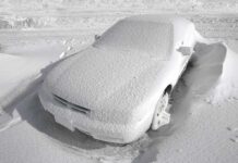 A car completely covered in snow, surrounded by a winter landscape