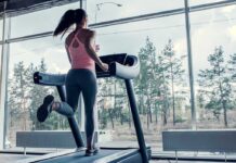 A woman running on a treadmill in a gym with large windows
