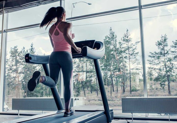 A woman running on a treadmill in a gym with large windows
