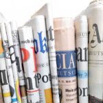 Massive Layoffs Hit Bezos’ Washington Post A collection of rolled newspapers displaying various headlines and designs