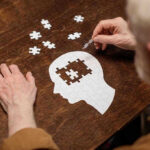 Elderly person completing head-shaped jigsaw puzzle.