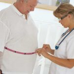 A healthcare professional measuring a patients waist with a tape measure