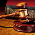 A wooden gavel resting on a polished surface with a law book in the background