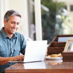 A man sitting at a desk working on a laptop with a smile