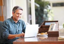 A man sitting at a desk working on a laptop with a smile