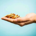 A hand holding a stack of gold coins against a light blue background