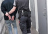 Fugitive CEO BUSTED in U.S. Army Camp! Officer escorting handcuffed person down hallway.
