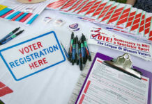 Epstein Doppelgänger Runs For Mayor Voter registration table with forms, pens, and brochures.