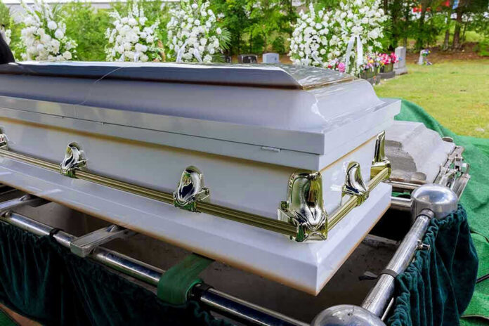 2198594525 White coffin with flowers in the background.