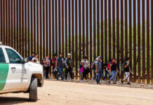 People walking beside tall fence and border patrol vehicle.