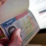 A hand holding an open passport displaying a visa page