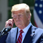 Federal Court Defies SCOTUS, Rules Trump Can’t Fire DEI Officers Man in a suit adjusting an earpiece.