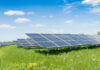 Big Tech Now GRABBING Native American Land! Solar panels in a grassy field under blue sky.