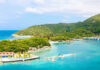 Americans Advised to NOT Travel Here! Tropical beach with docks and lush green hills.