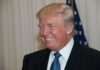 Trump Shares HILARIOUS Moment With VP’s Wife! A smiling man in formal attire with an American flag in the background