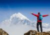 Hiker with arms raised facing snowy mountain peak
