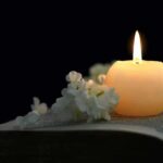 TV Icon Found DEAD Inside Home Candle on an open book with white flowers