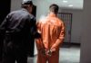 Man ARRESTED With Body Parts Entering Country Illegally Police officer escorting handcuffed inmate in orange jumpsuit