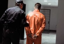 Man ARRESTED With Body Parts Entering Country Illegally Police officer escorting handcuffed inmate in orange jumpsuit
