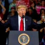 Donald Trump speaking at a rally podium with arms raised