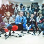 Famed CBS Anchor Fired After Leadership Showdown! Row of microphones at a press conference with audience and cameras behind