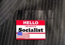 Socialist Slate Rising – Midterms Getting Wild Name tag on a pinstripe suit jacket pocket
