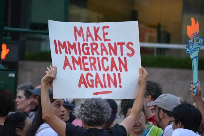 shutterstock_1449371015 Teddy Williams at a protest holding a sign reading 'Make Immigrants American Again'