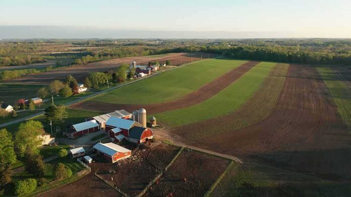 shutterstock_1737529889 Aerial view of a farm with red barns and expansive green and brown fields