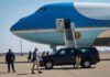 Zelenskyy’s Plane Struck By Drone Amid Takeoff Security detail near blue and white aircraft with staircase and SUV