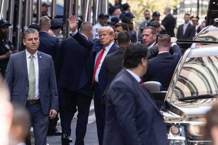 shutterstock_2284766695 Donald Trump waving while surrounded by security personnel on a city street