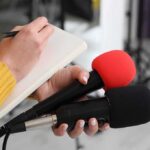 Brand-New Rollercoaster STOPS Mid-Air, People Stranded! Journalist holding two microphones while writing in a notebook